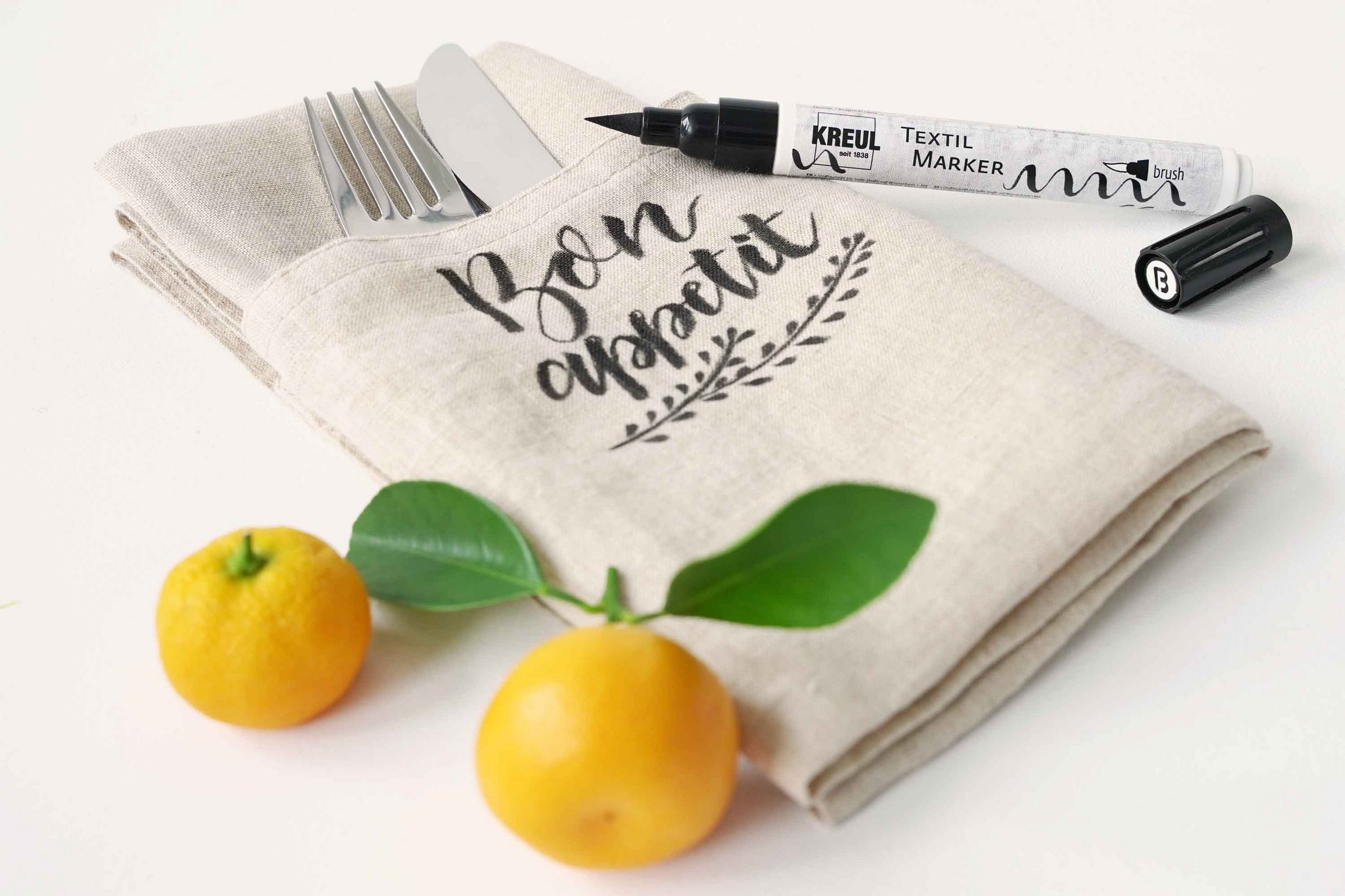 Stoffserviette bemalt mit Schriftzug Bon Appetit KREUL Textil Marker und Orangen daneben