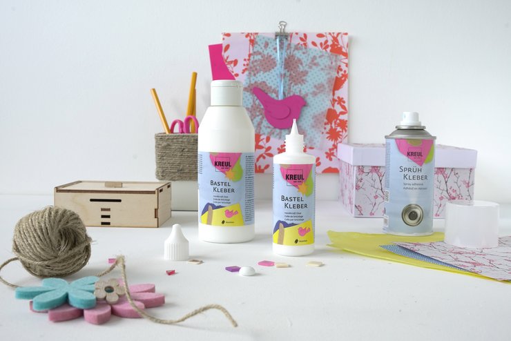 KREUL Bastel Kleber FAQ Fragen Antworten Tipp Anwendung Alleskleber Universalkleber Flaschen KREUL Bastelkleber stehen vor Bastelmaterialien