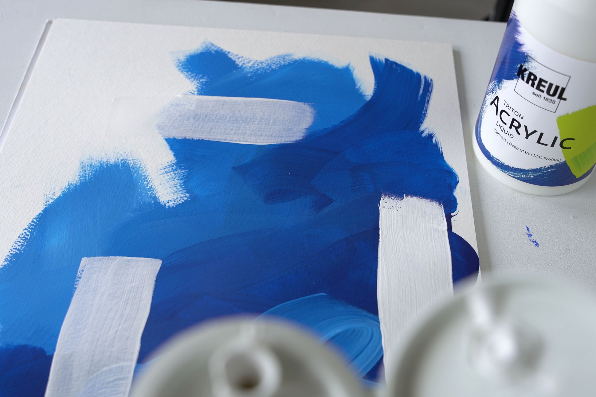 KREUL Triton Acrylic Liquid Mischweiß Flasche neben einer Leinwand mit Weiß Aufstrichen