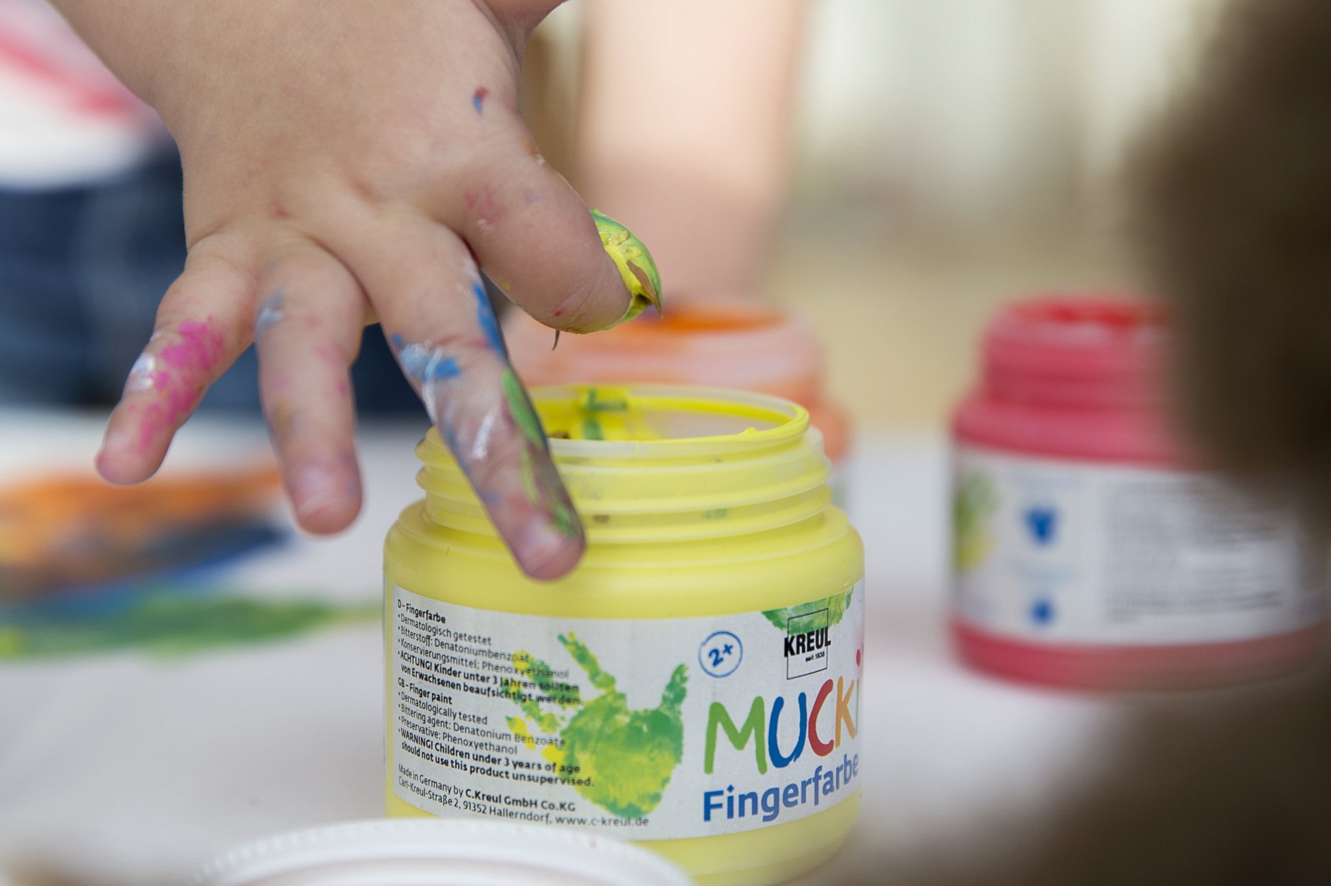 Altersempfehlung ab 2 Jahren MUCKI Fingerfarbe Kinderhand taucht in gelbe MUCKI Fingerfarbe