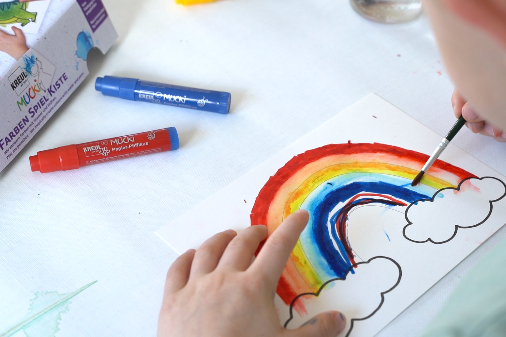Kind malt mit Aquarellstiften einen Regenbogen