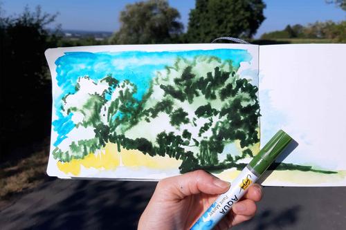 Baum Skizze in Skizzenbuch vor Landschaft mit Stift