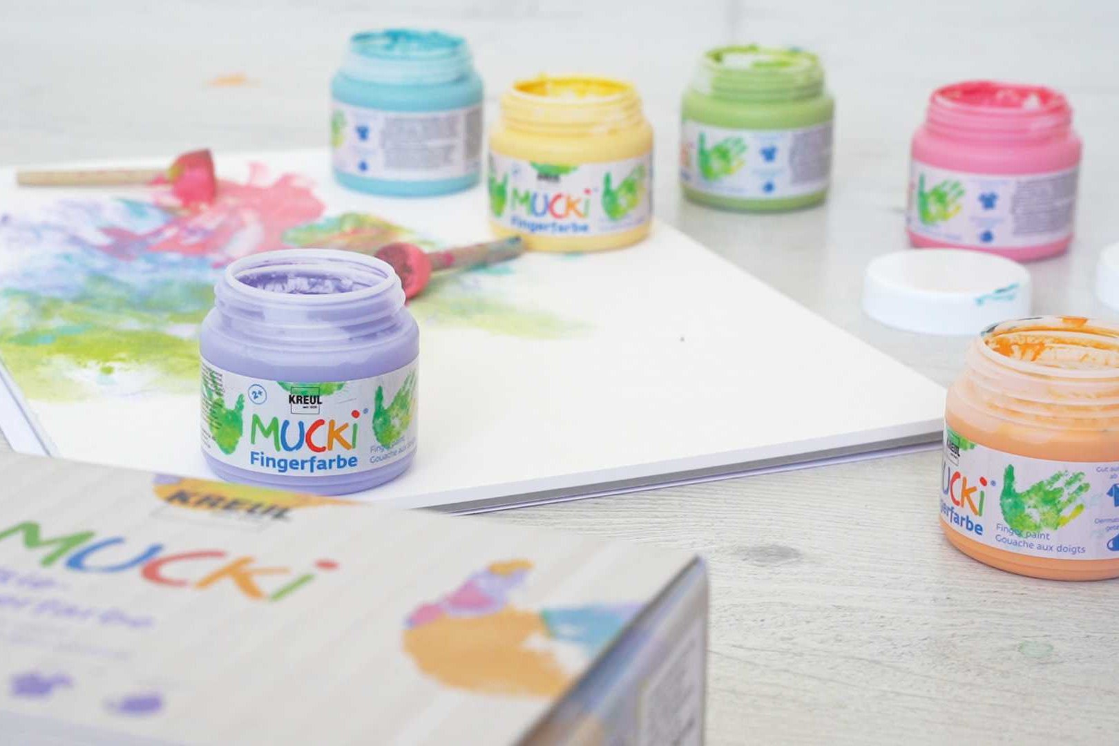MUCKI Fingerfarbe sicher unbedenklich vegan parabenfrei laktosefrei glutenfrei MUCKI Fingerfarbe Farbdosen und Malblock auf dem Boden