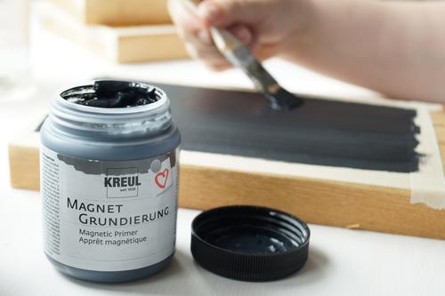 Dose mit KREUL Magnetgrundierung neben Holzbrett auf dem die schwarze Grundierung mit Pinsel aufgetragen wird