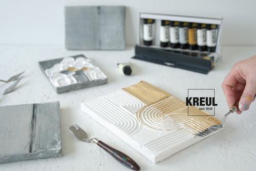 Eine Hand streicht mit dem geriffelten Malmesser Strukturpaste auf einen Keilrahmen