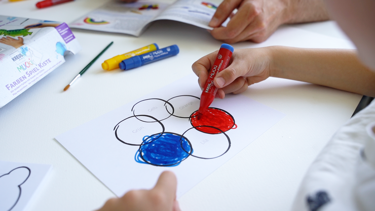 Kinderhände malen mit Stift einen Farbkreis