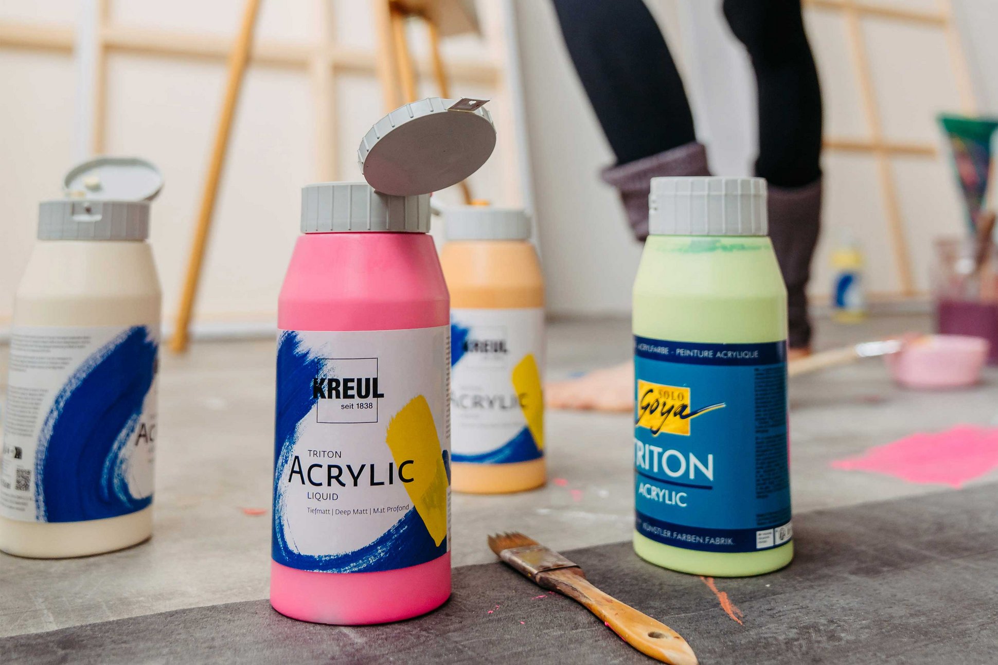 KREUL Triton Acrylic neues Design klare Kommunikation neuer Name Fokus auf Nachhaltigkeit KREUL TRiton Acrylic Liquid Farbflasche auf dem Boden eines Ateliers neben SOLO GOYA Triton Acrylic