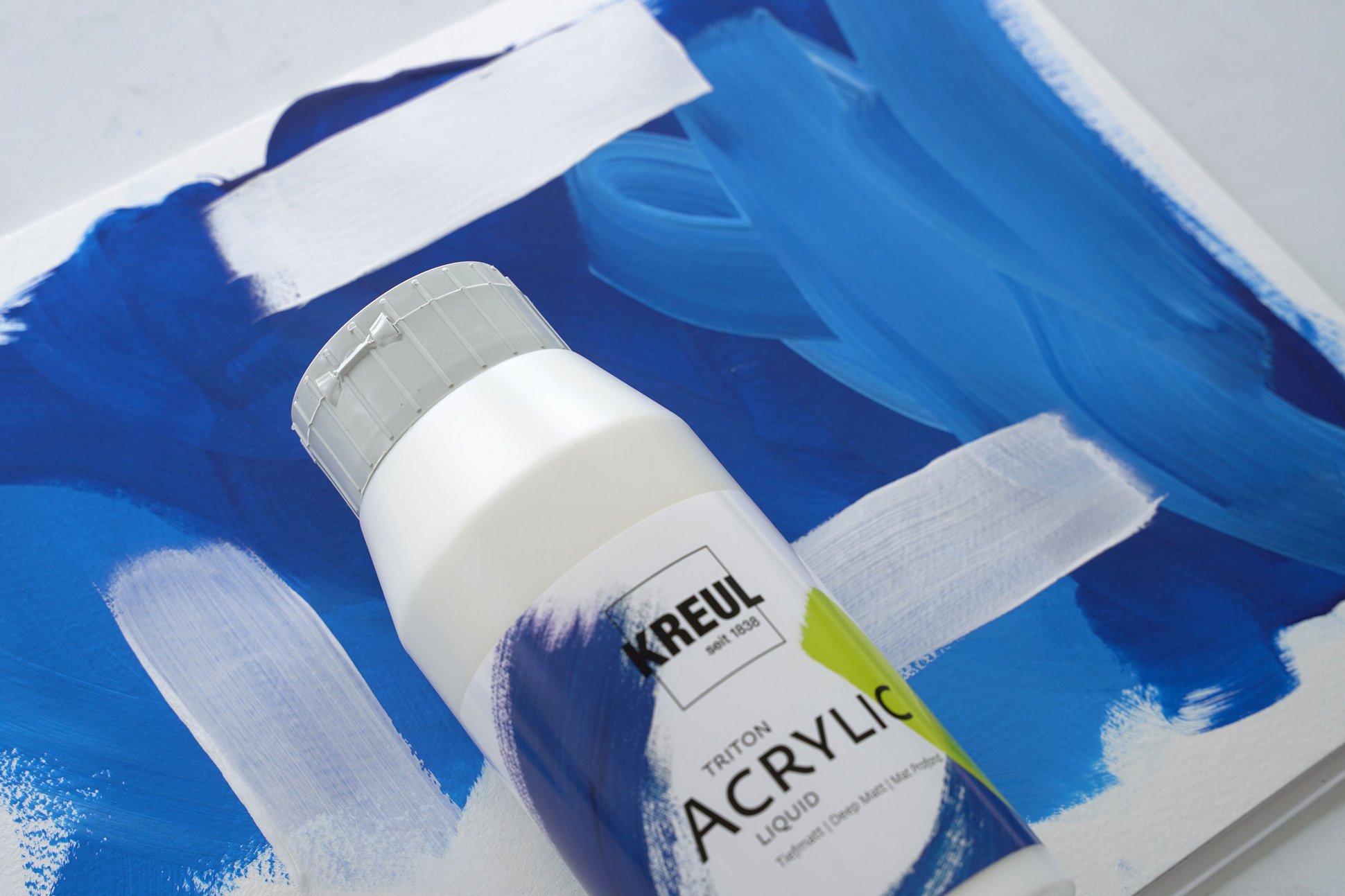 Farbflasche mit KREUL Triton Acrylic Liquid Weiß auf einer Leinwand mit weißen Farbaufstrichen