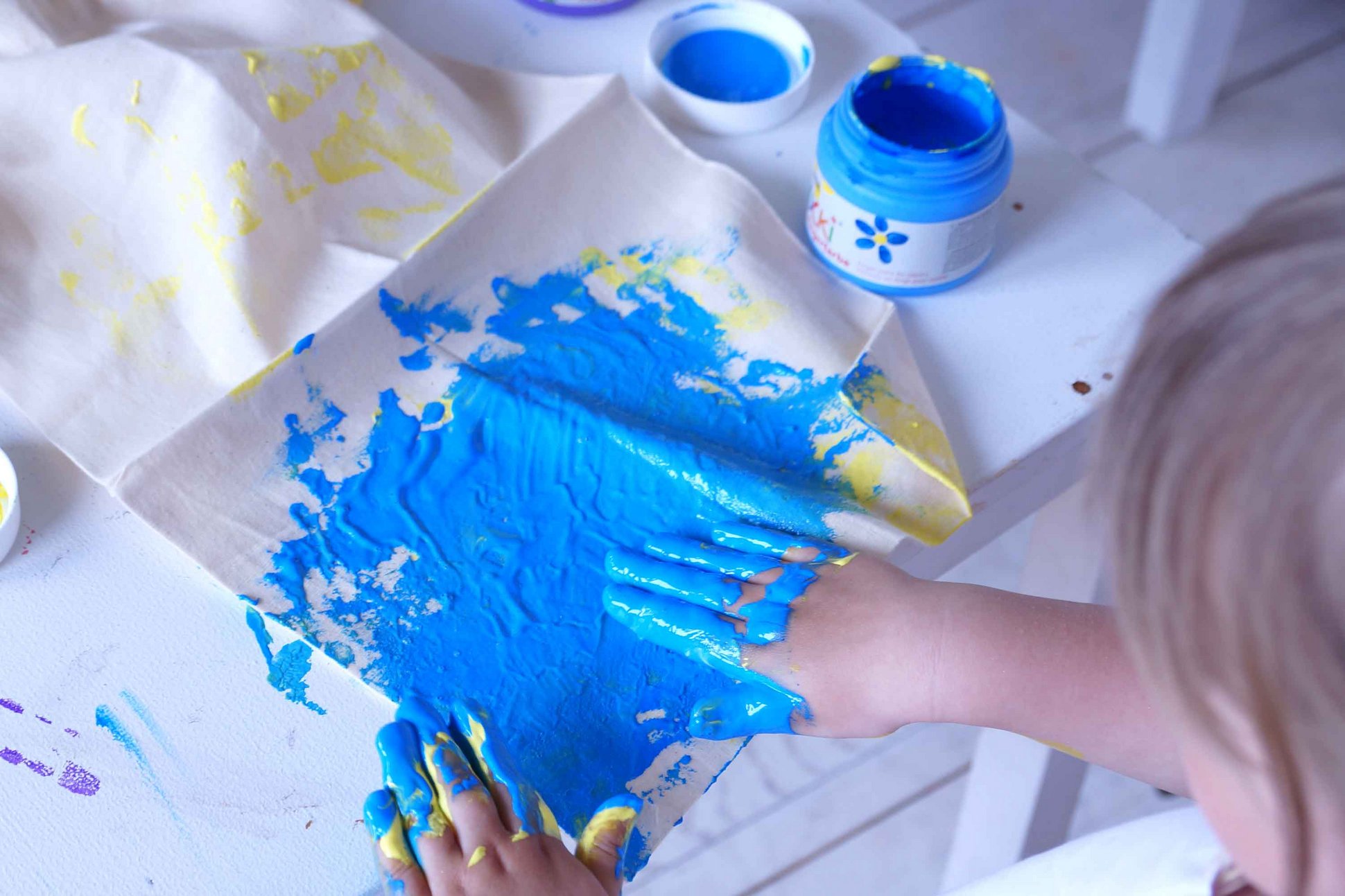 Kind malt mit blauer Stoff Fingerfarbe auf Stoff mit den Händen
