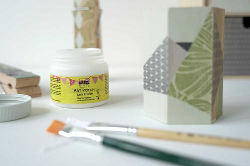 Dose mit KREUL Art Potch, Pinsel, Serviette und mit Serviette beklebte Ordnungshelfer auf einem Tisch