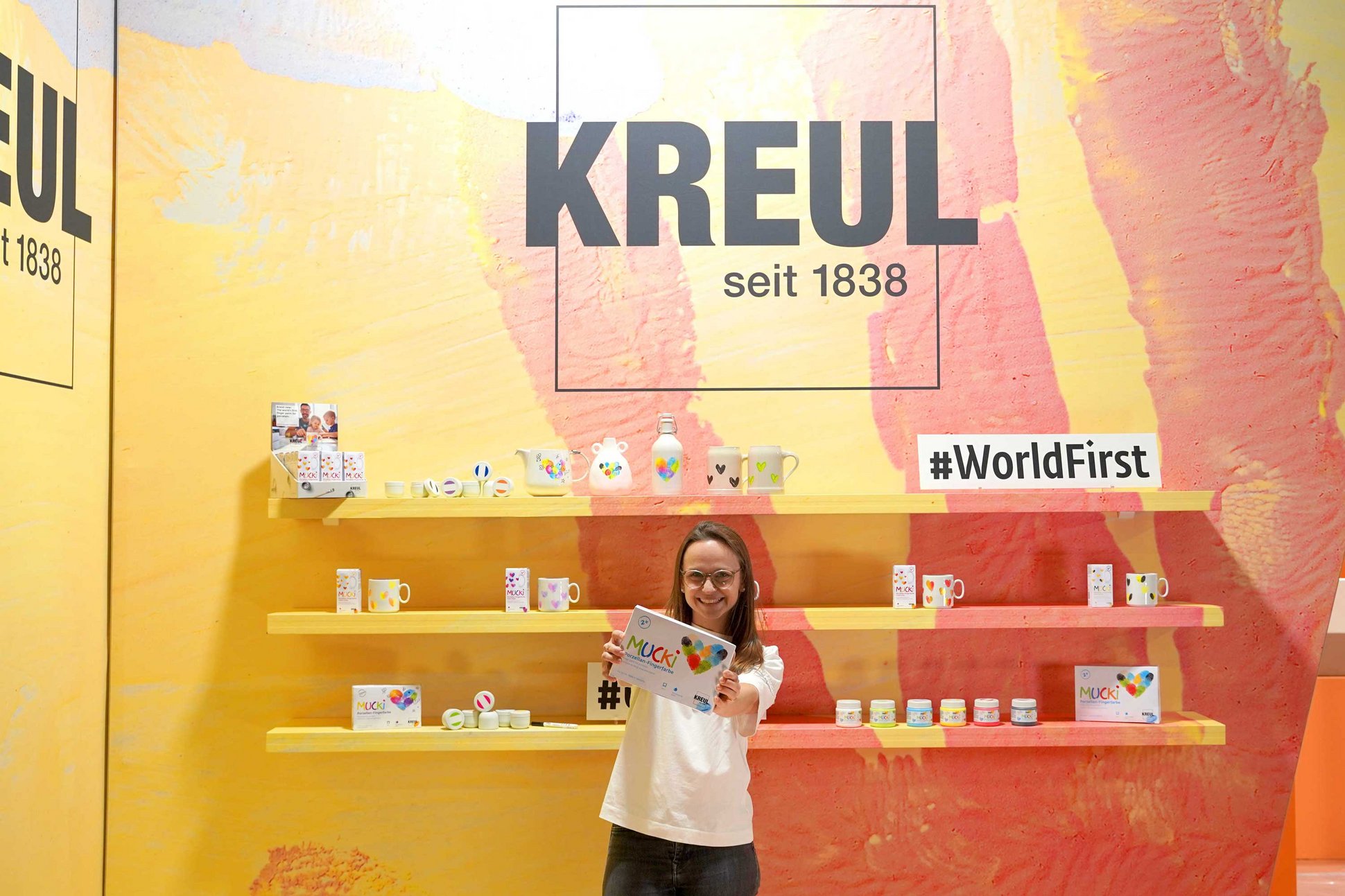Frau mit MUCKI Fingerfarbe vor Regal mit Fingerfarbe