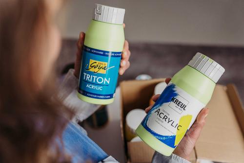 SOLO GOYA Triton Acrylic Farbflasche neben KREUL Triton Acrylic Liquid Farbflasche in den Händen einer Frau